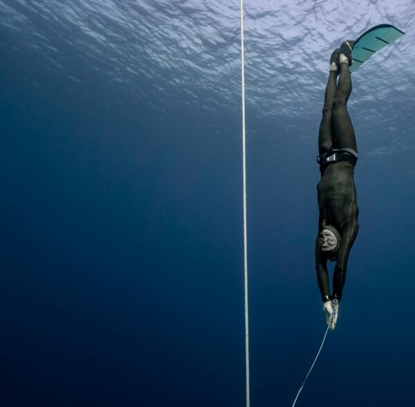 Full body of sporty male swimmer in black swimsuit diving in deep turquoise water of magnificent ocean